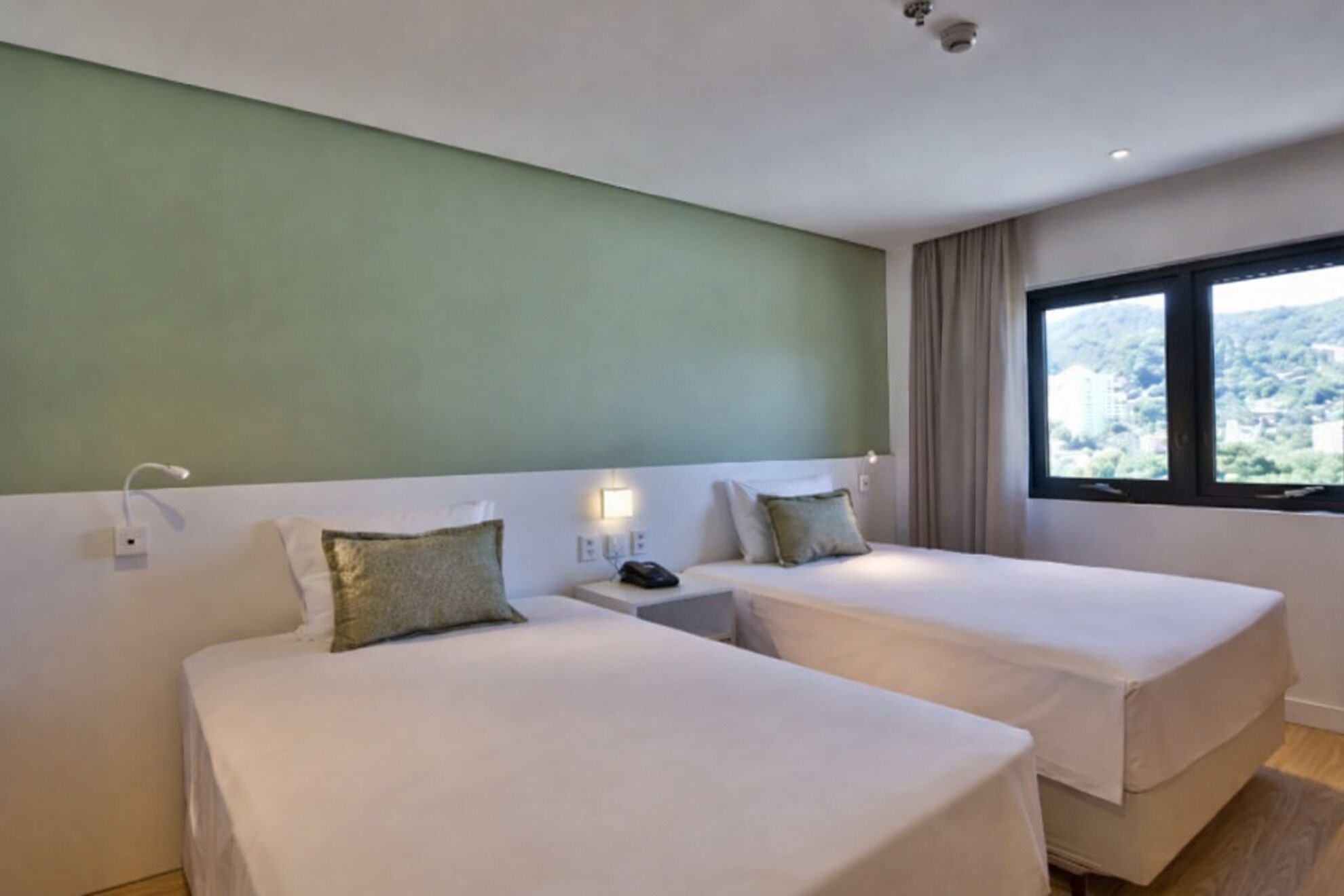 A hotel room with two beds, a nightstand with a phone, and a window with a view of a mountainous landscape.