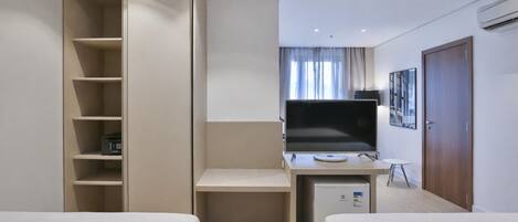 A hotel room with two beds, a desk with a computer, a TV, a wardrobe, and an air conditioning unit.