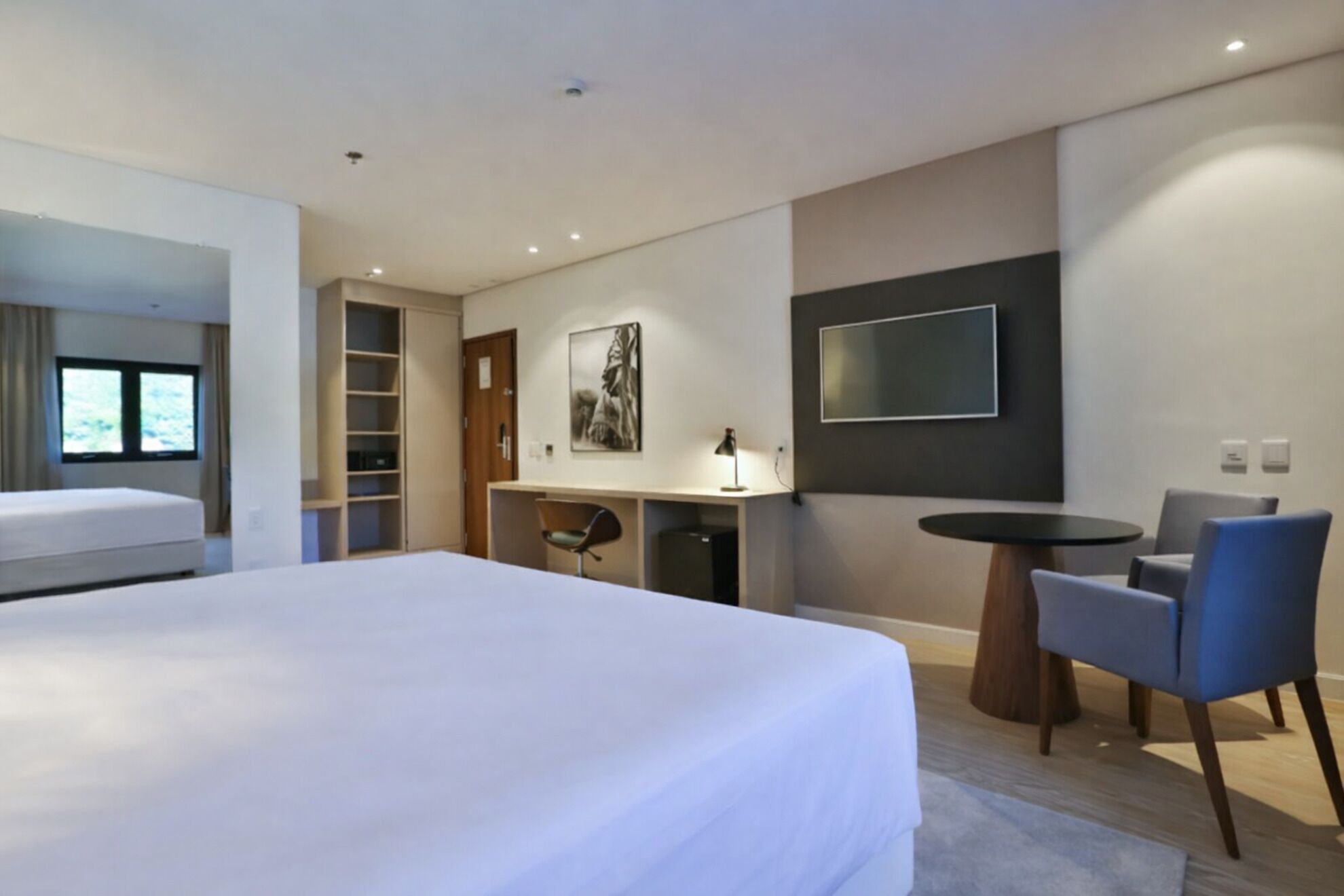 Ett modernt hotellrum med en stor säng, ett skrivbord, en stol, en TV och en bokhylla.