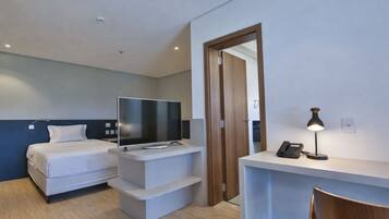 A modern hotel room with a bed, a TV on a stand, a desk with a phone, and a chair.