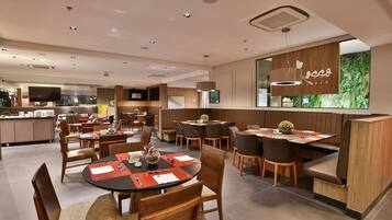 A modern restaurant with round tables, booths, and a large TV screen.