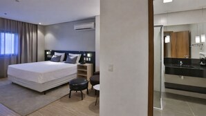Una habitación de hotel moderna con una cama grande, una mesita de noche, un taburete pequeño, un escritorio y un baño con espejo y lavamanos.
