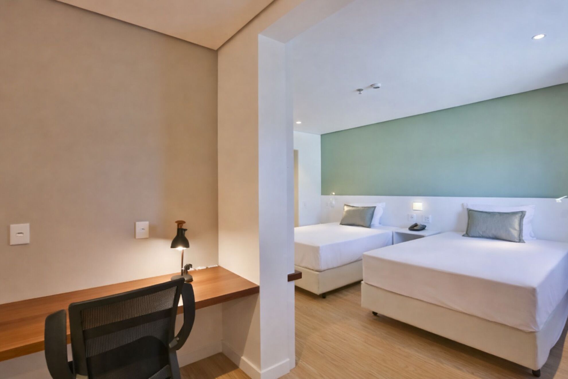 A hotel room with two beds, a desk, and a chair.