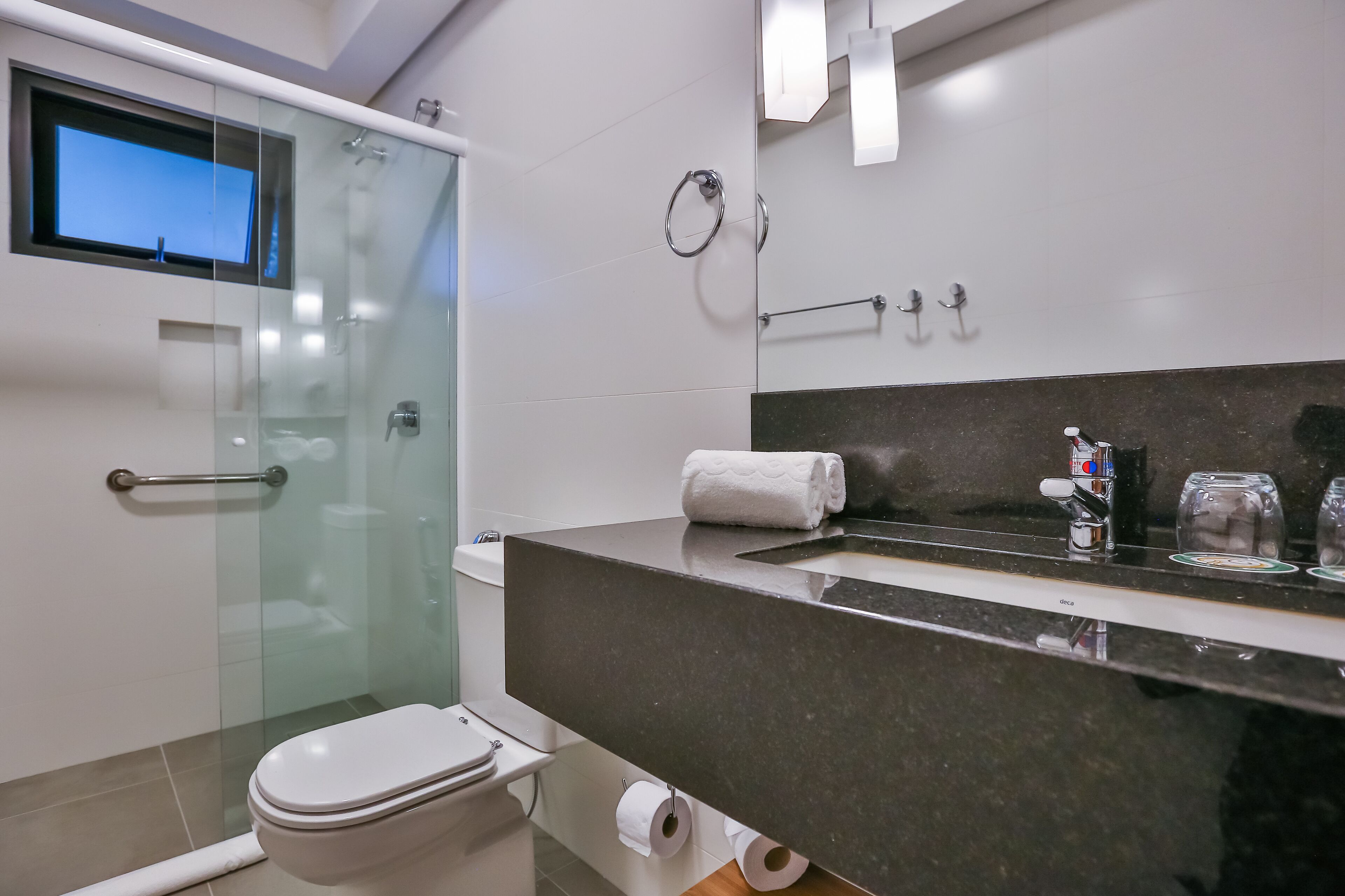 Et moderne badeværelse med brusekabine i glas, toilet, vask med mørk bordplade og spejl.