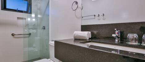 Un baño moderno con cabina de ducha de vidrio, inodoro, lavabo con encimera oscura y espejo.