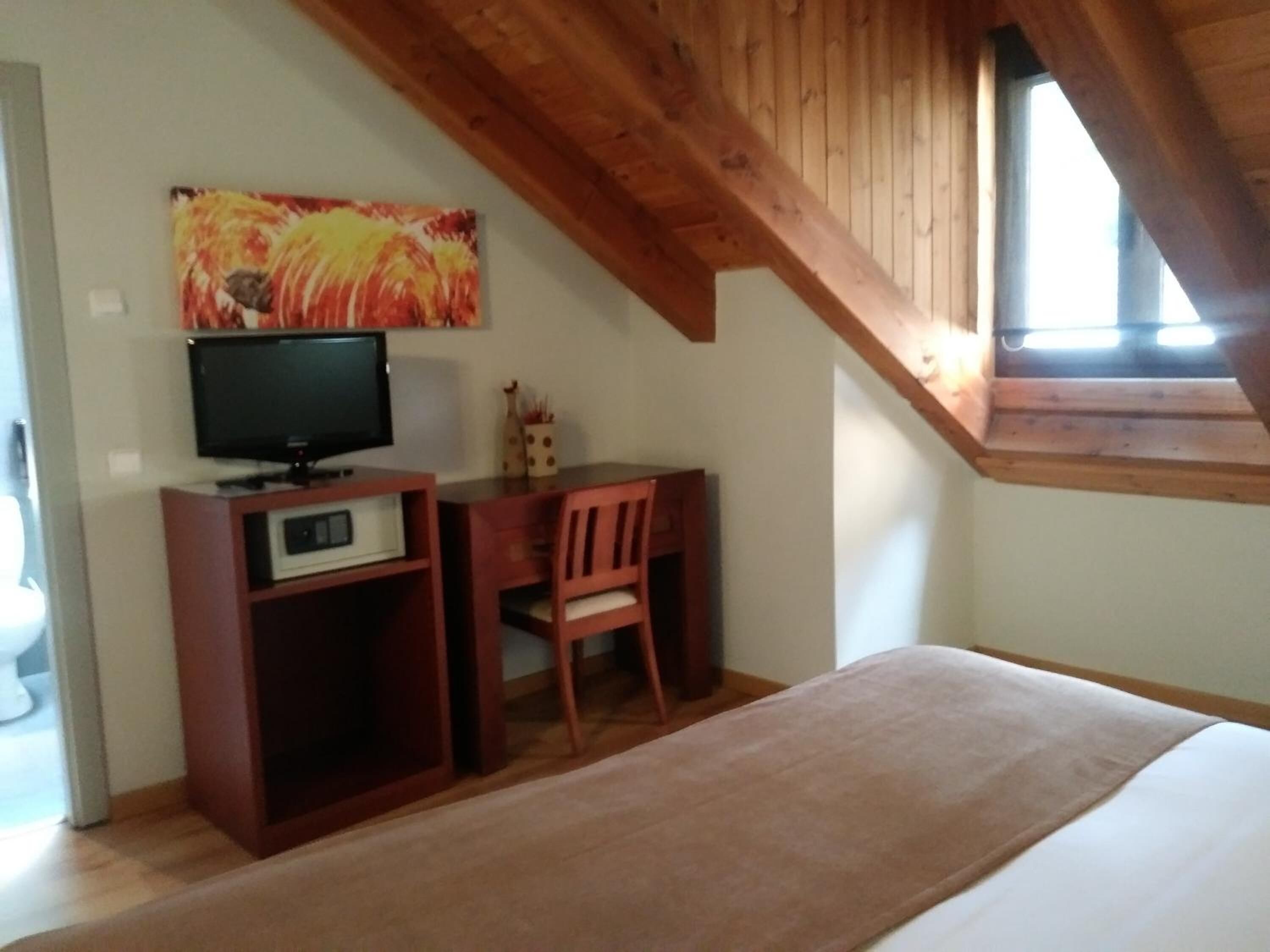 Un dormitorio con un escritorio de madera, una silla, un televisor y un cuadro en la pared.