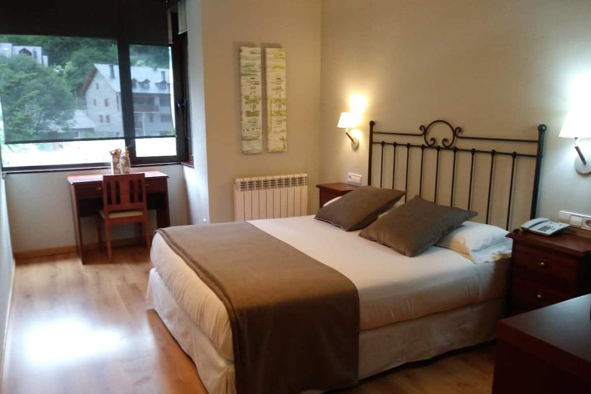 A bedroom with a bed, bedside table, lamp, and a desk with a chair.