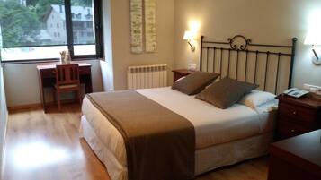 A bedroom with a bed, bedside table, lamp, and a desk with a chair.