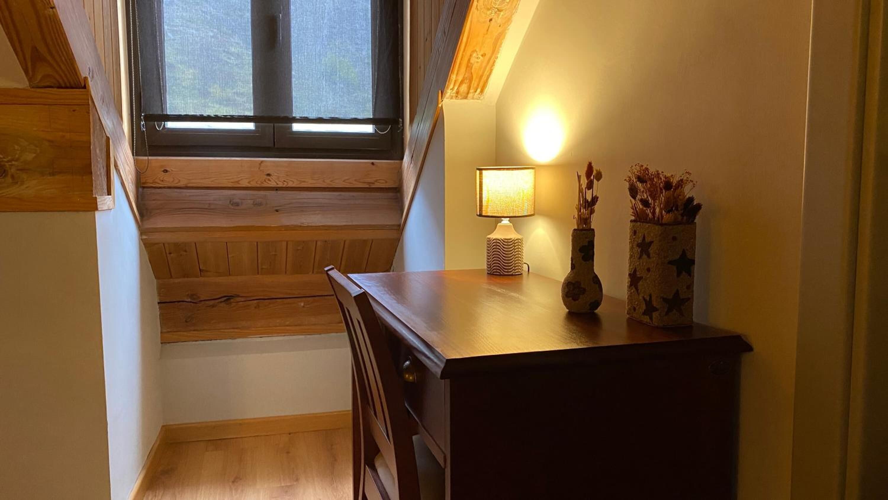 Una escalera de madera que lleva a un rellano con un escritorio y una lámpara.