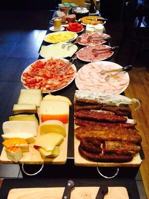 A buffet table with various cheeses, meats, and fruits.