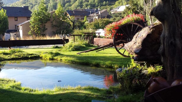A rural setting with a pond, a wooden bridge, and a water wheel. - Roca Blanca (Espot)