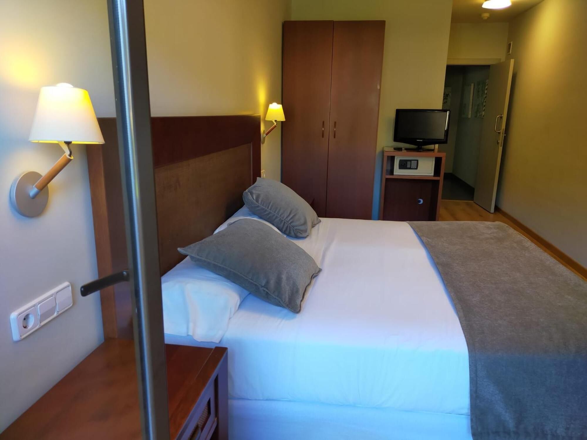 Een hotelkamer met een bed, nachtlampjes, een kledingkast, een televisie en een klein tafeltje.
