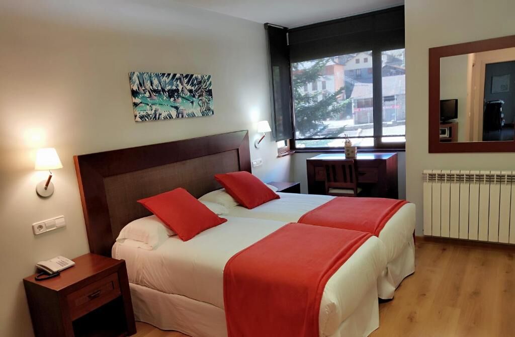 A hotel room with two beds, a desk, a chair, a lamp, a painting, and a window with a view.