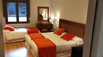 A hotel room with two beds, each with red pillows and white bedding. There is a wooden dresser with a mirror and two wall-mounted lamps.