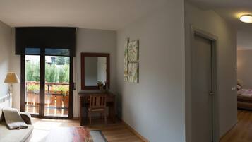A room with a sofa, a desk, a chair, a bed, and a balcony with plants.
