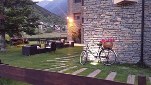 A stone building with a bicycle and basket, surrounded by a well-maintained lawn and outdoor seating area. - Roca Blanca (Espot)