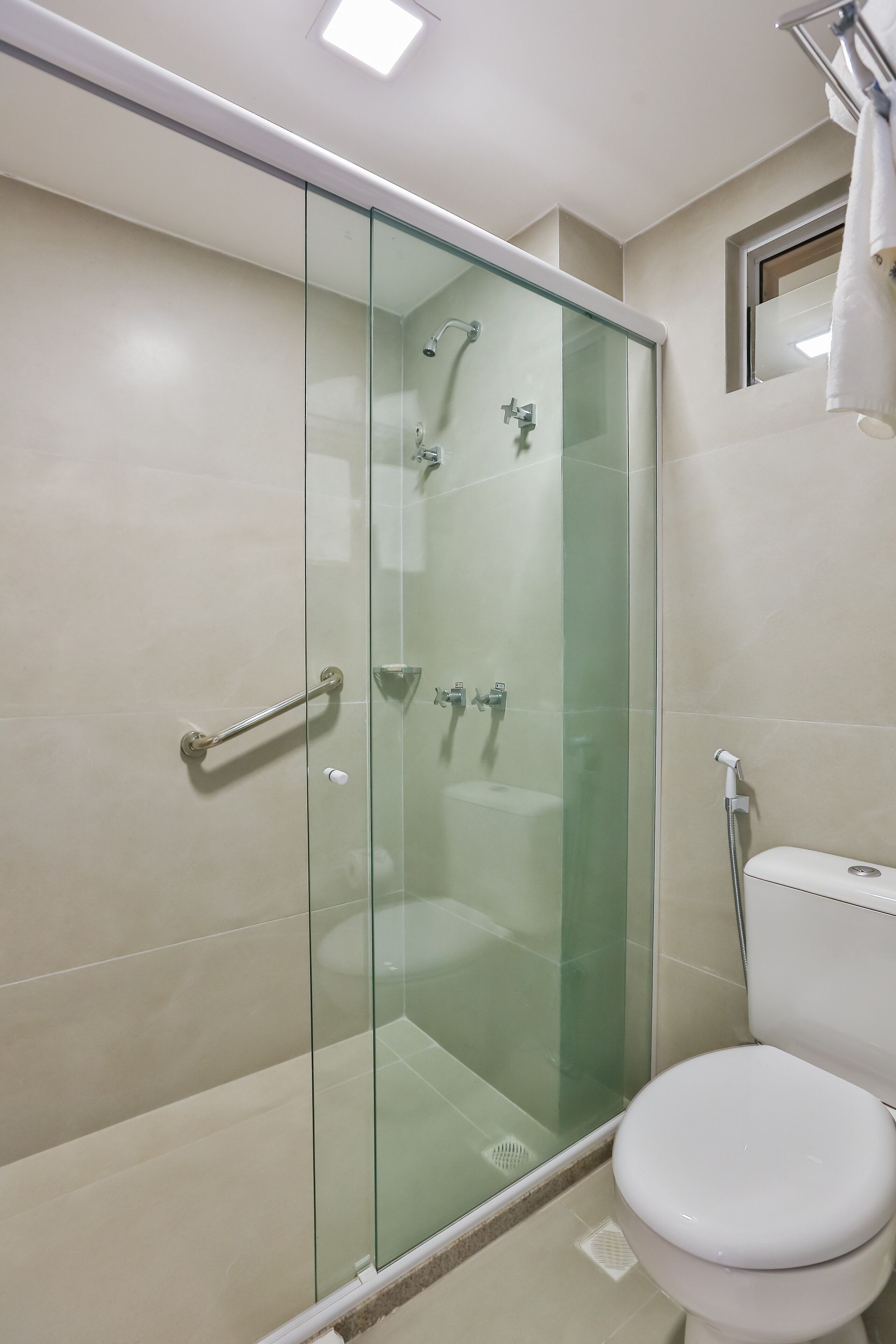 A modern bathroom with a glass-enclosed shower, a white toilet, and a small window above the mirror.