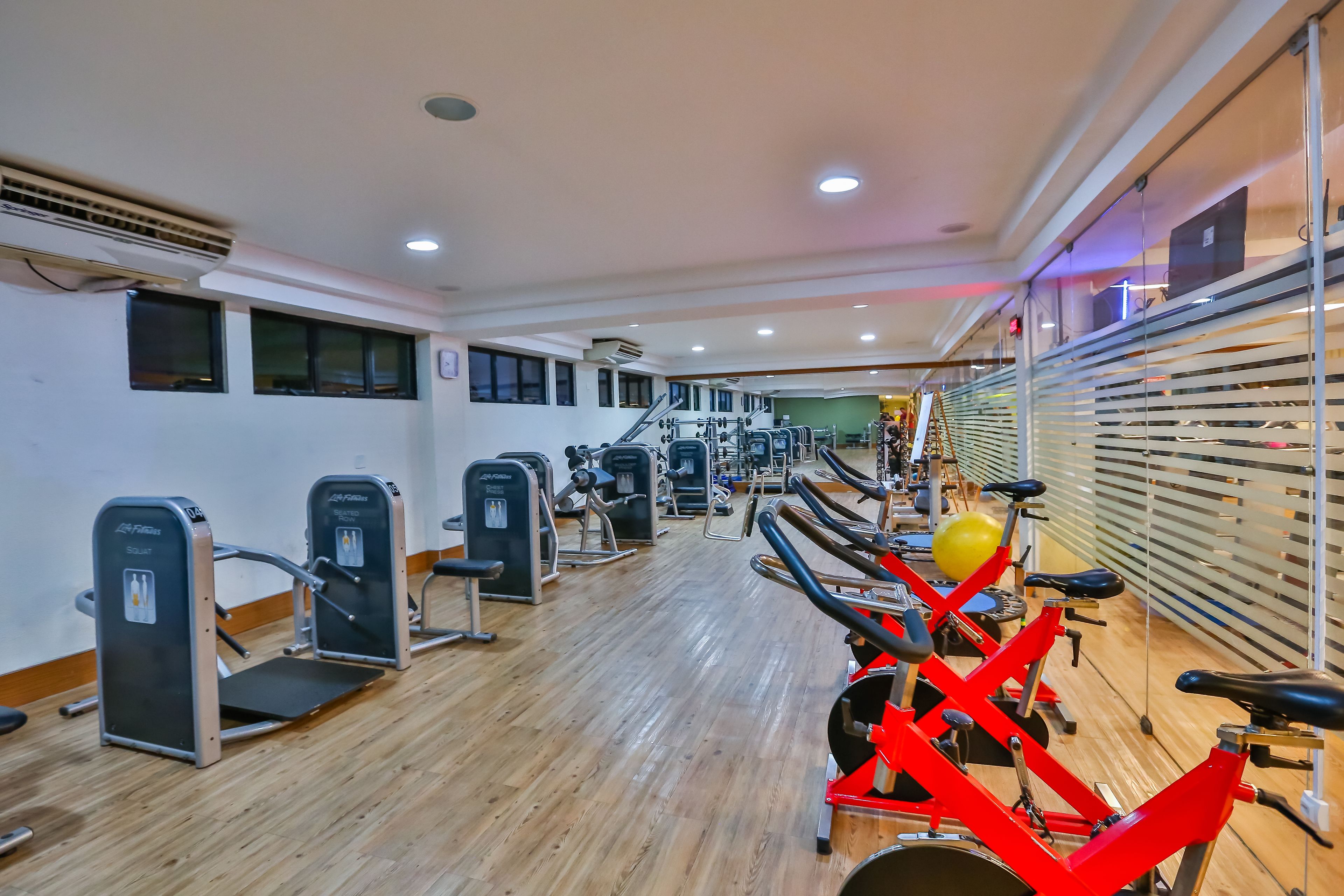 Un gimnasio con máquinas de cardio, estaciones de pesas y suelo de madera.