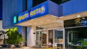 Entrada de hotel com uma placa indicando "Quality Suites" e uma recepção visível.