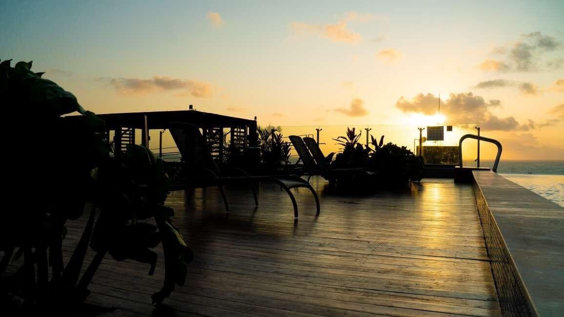 A wooden deck with lounge chairs and a small structure, overlooking a body of water at sunset.