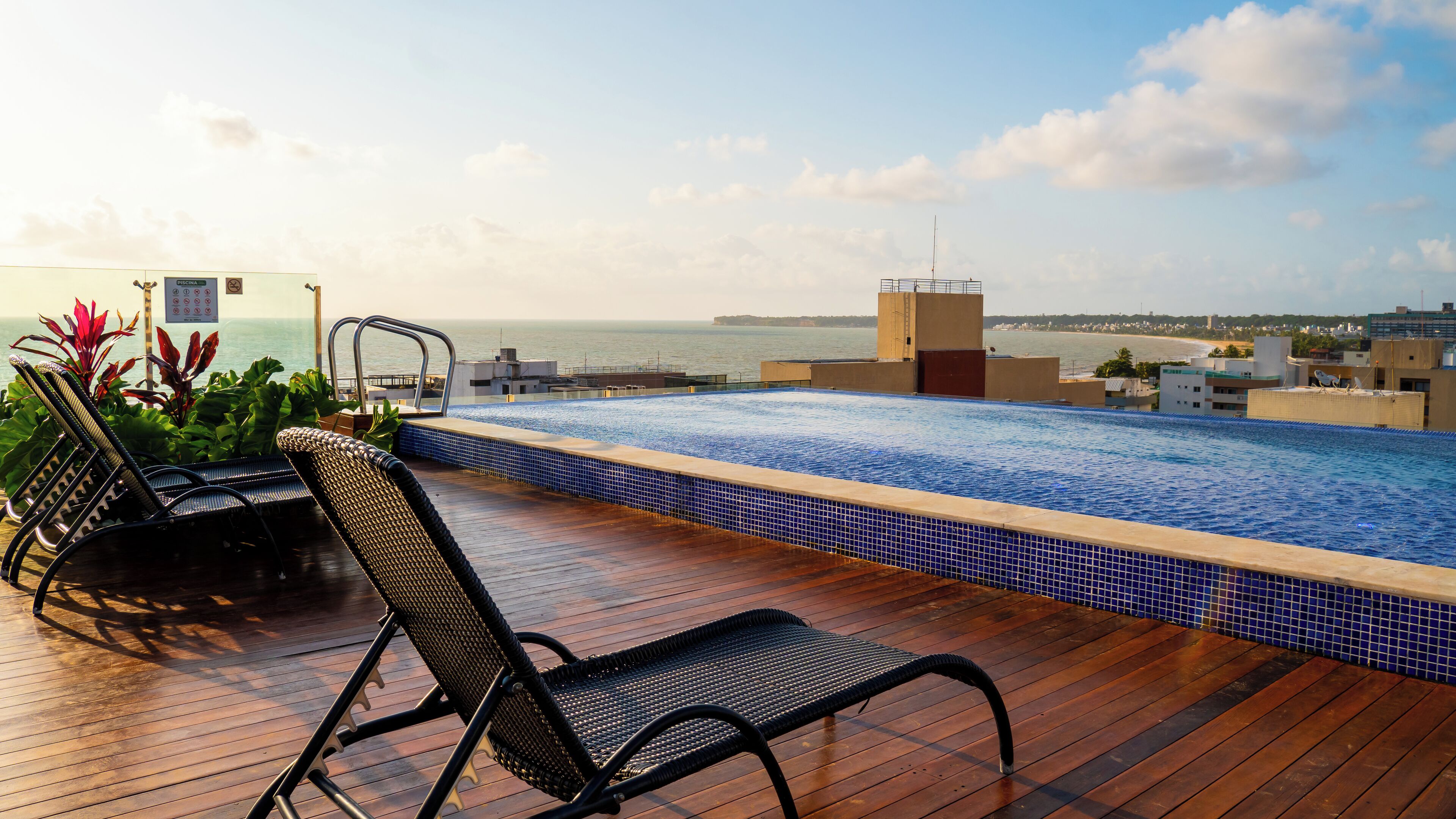 Ein Pool auf dem Dach mit Blick auf den Ozean, Liegestühlen und einer gefliesten Terrasse.