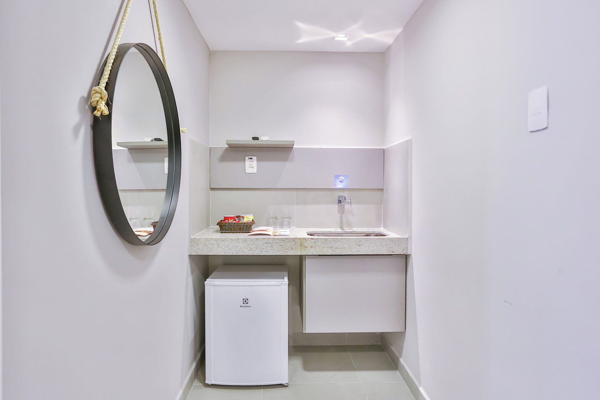 A compact bathroom with a white sink, a mirror, a small refrigerator, and a towel rack.