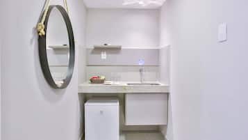 A compact bathroom with a white sink, a mirror, a small refrigerator, and a towel rack.