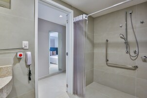 A modern bathroom with a shower, a handrail, and a phone on the wall.