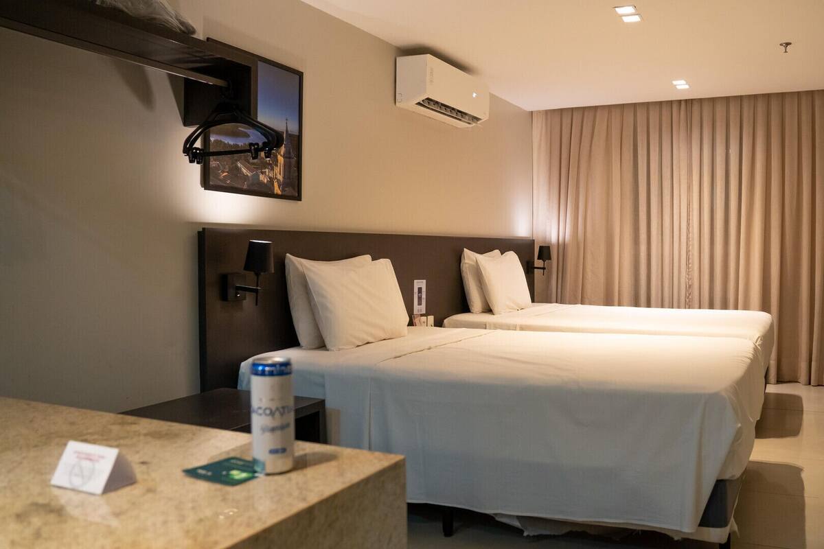 A hotel room with two beds, a desk with a chair, a mounted TV, and a window with curtains.