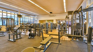 Uma academia com diversos equipamentos de exercícios, janelas amplas e pé direito alto.