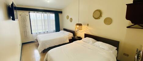 A hotel room with two beds, a ceiling fan, a hanging light fixture, and a view of the outdoors through a window.