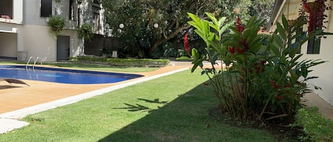 A swimming pool with a tiled deck, surrounded by well-maintained grass and various plants.