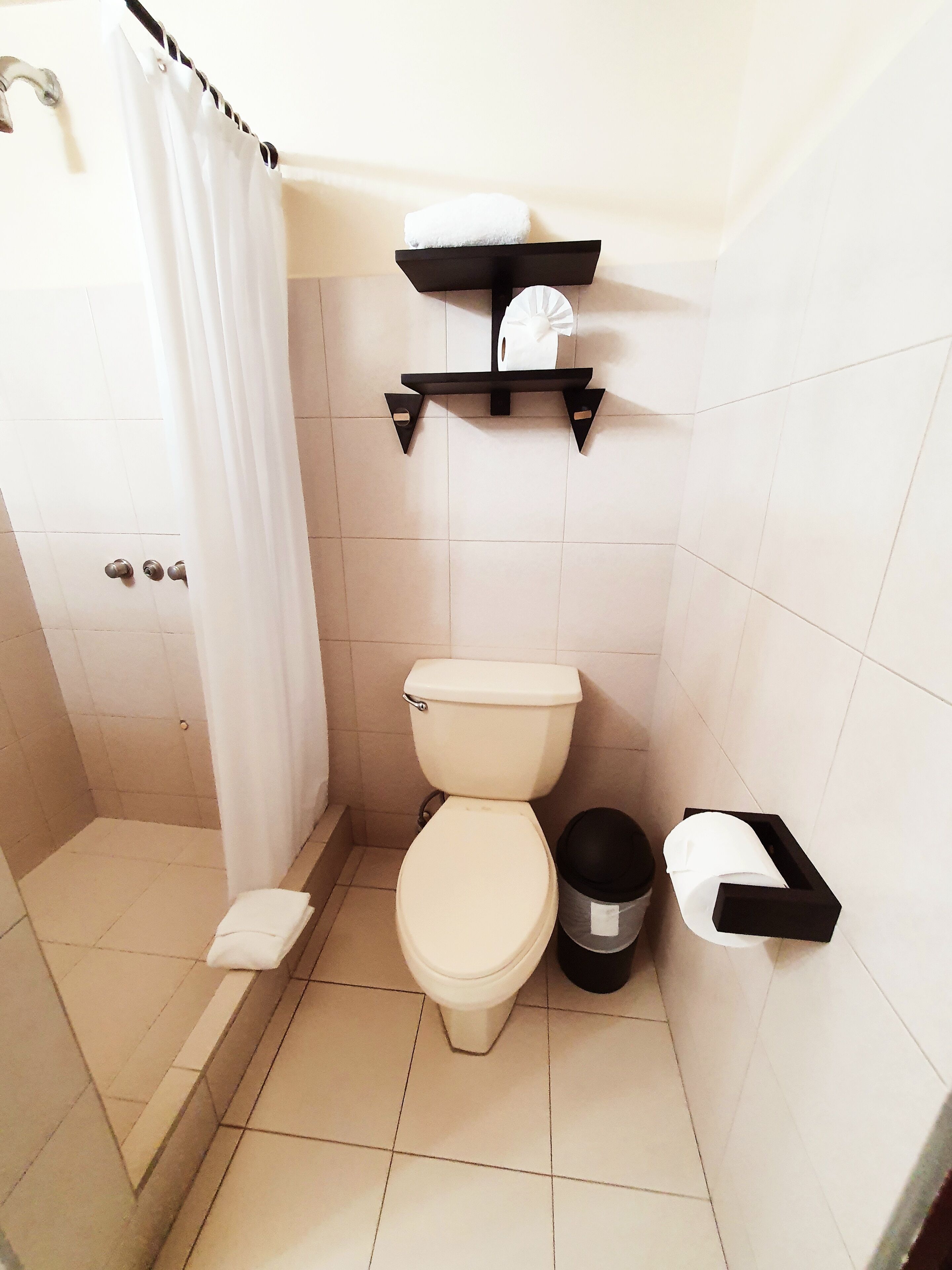 Un baño con inodoro, ducha, toallero y cubo de basura.
