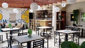 A restaurant with multiple tables and chairs, a bar area, and hanging plants. - Hotel Mango (Rio Segundo)
