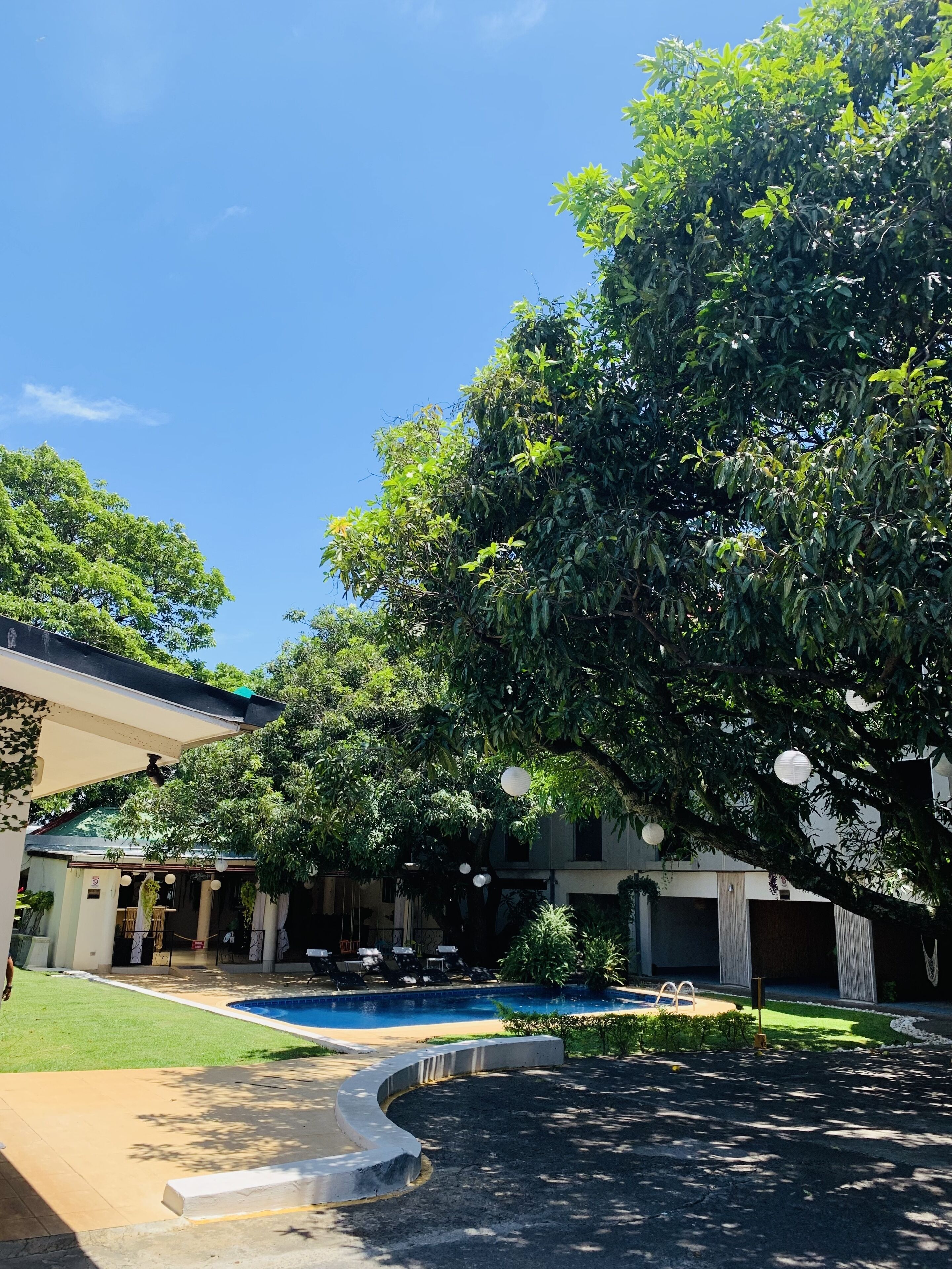 A pool area with a clear blue sky, surrounded by lush greenery and a covered seating area.