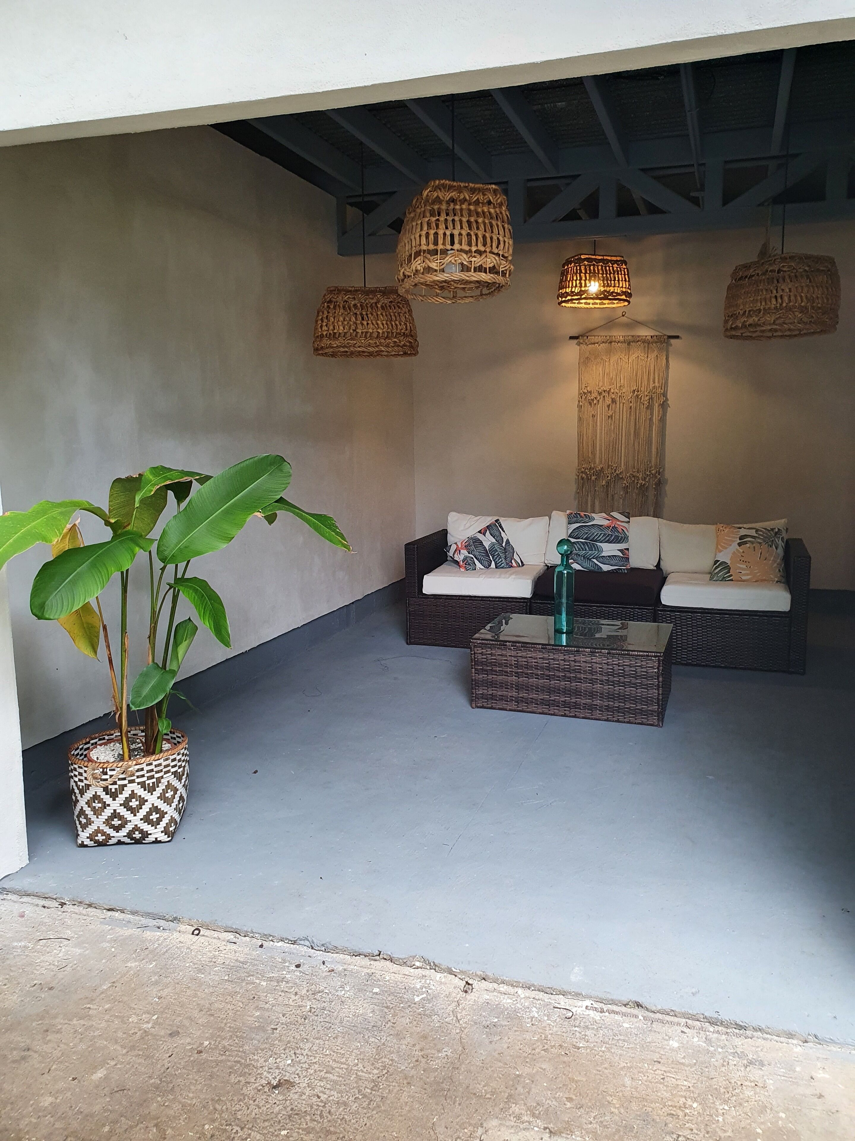 A cozy seating area with wicker furniture and hanging lights, a potted plant, and a textured wall.