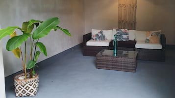 A cozy seating area with wicker furniture and hanging lights, a potted plant, and a textured wall.