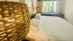 A bedroom with a bed, a woven chair, a macrame wall hanging, and a window with curtains. - Hotel Mango (Rio Segundo)