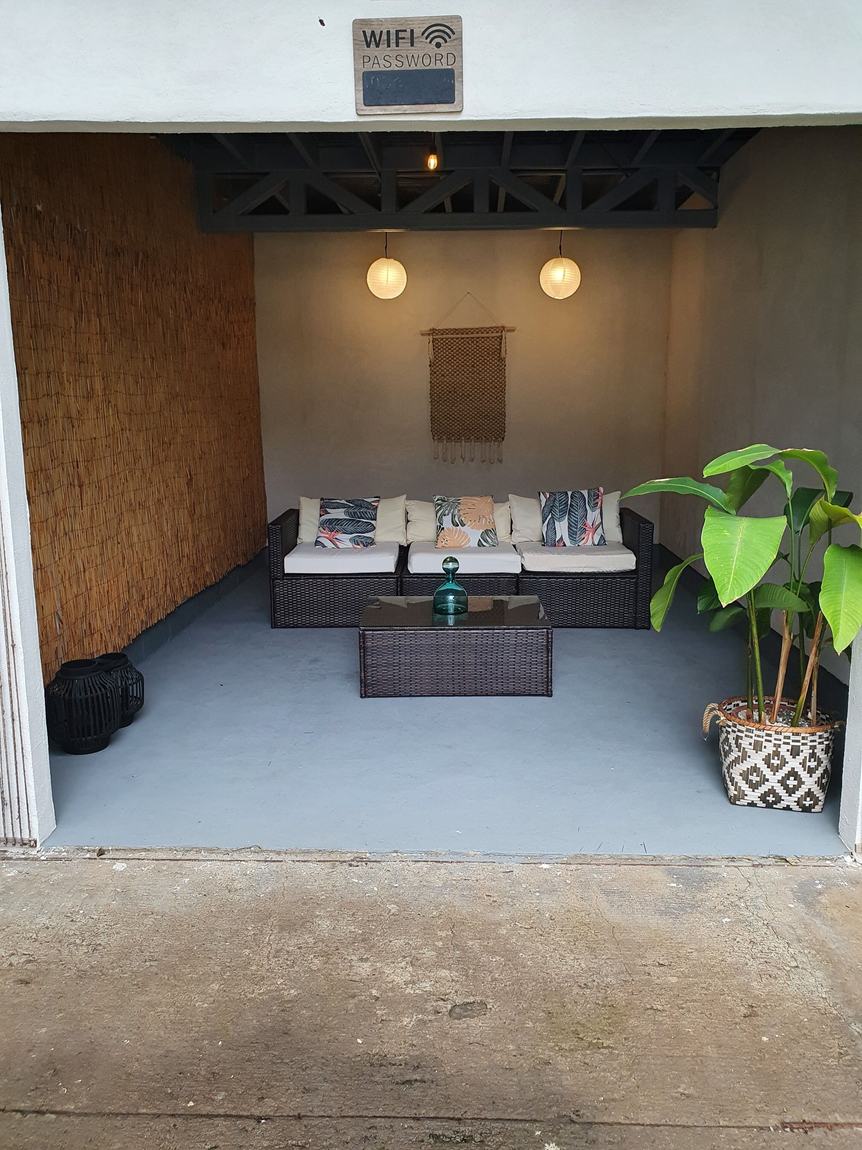Un área de estar exterior acogedora con un sofá, dos lámparas colgantes, una mesa de centro tejida y una planta en maceta.