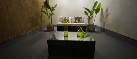 Quarto moderno com mesa de centro de vidro, duas plantas em vasos, um sofá com almofadas estampadas e um lustre.