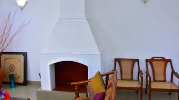 Una habitación con chimenea, dos sillas de madera con asientos de mimbre y un jarrón con flores.