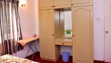 A bedroom with a bed, an ironing board, a wardrobe, a mirror, and a laundry basket.