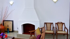 A living room with a fireplace, two wooden chairs, a vase with flowers, and wall-mounted lights.