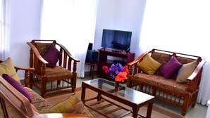 A living room with wooden furniture, a glass coffee table, and a TV on a stand.