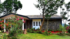 A house with a stone facade, a red roof, and a garden with pink flowers.