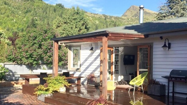 A house with a covered patio, outdoor seating, and a view of a forested hillside. - Arrowtown Gem - Pet Friendly Arrowtown Cottage. (Arrowtown)