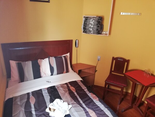 A hotel room with a bed, a bedside table, a chair, and a small table with a red tablecloth.