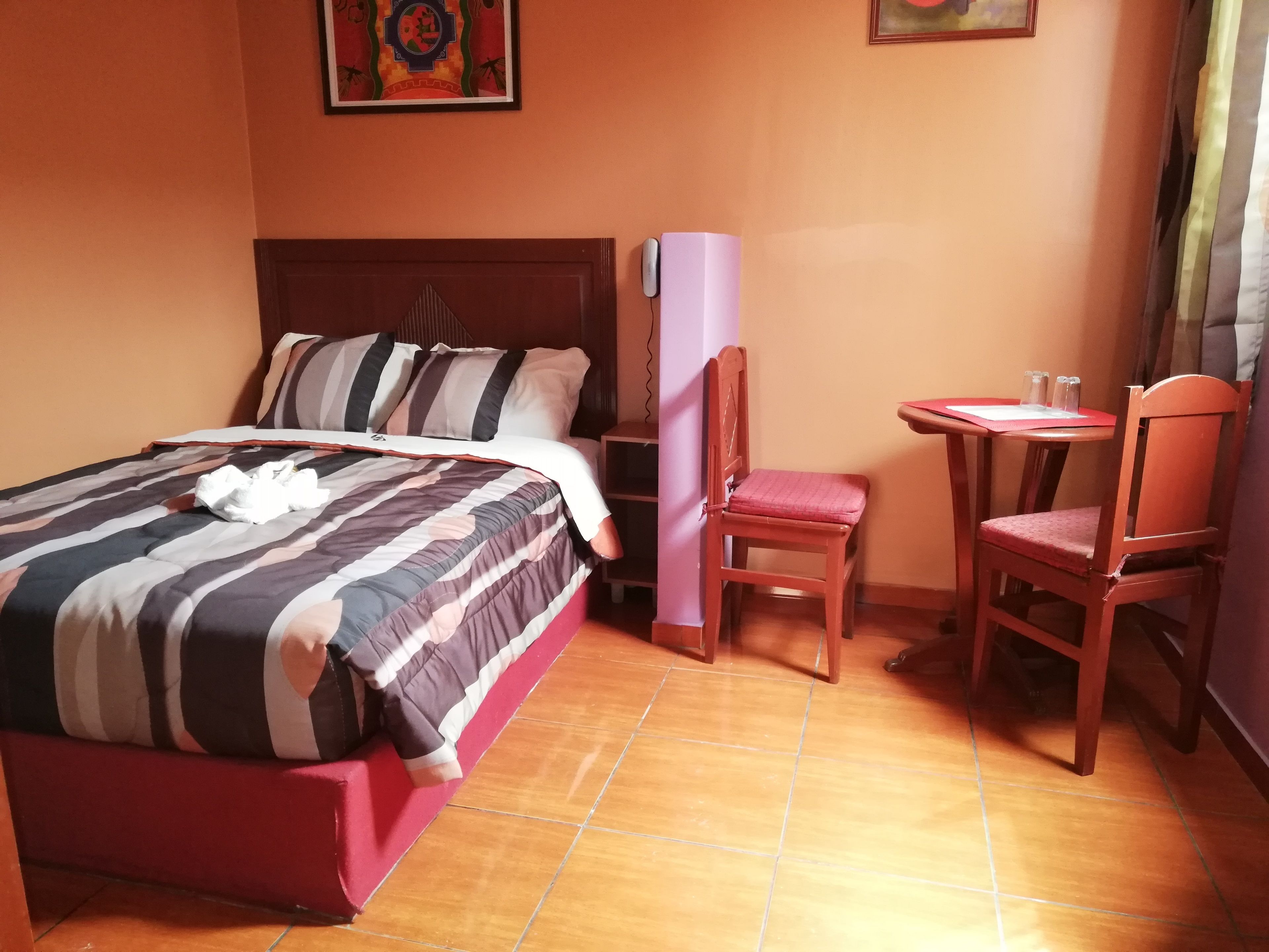 A hotel room with a bed, a chair, a small table, and a wall-mounted shelf.