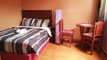 A hotel room with a bed, a chair, a small table, and a wall-mounted shelf.