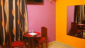 A room with a bed, a table with chairs, a television, and a wall-mounted fan.